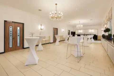 Tagungsraum IX (Bistro) – Elf Stehtische zum Teil mit Barhockern, zwei Kronleuchter, Wandleuchten, Fliesenboden, drei Doppeltüren links, Fenster rechts