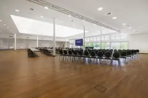 CongressCentrum – Weitwinkelansicht. Zwei Bestuhlungsbereiche: Reihenbestuhlung rechts, parlamentarisch links, LED-Display, Fensterfront zum Landschaftsschutzgebiet, Traversensystem, Oberlicht, Holzboden