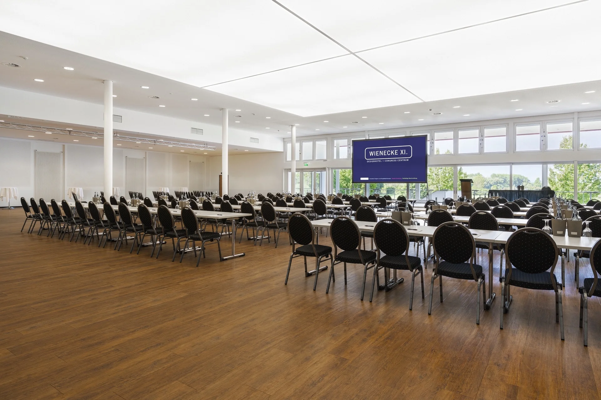 CongressCentrum – Nahaufnahme. Parlamentarische Bestuhlung mit Polsterstühlen, LED-Display, Fensterfront zum Landschaftsschutzgebiet, Oberlicht, Holzboden