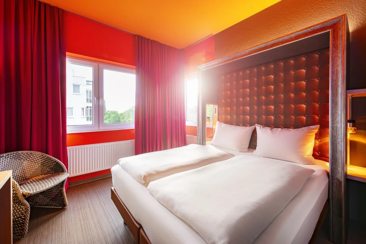 Doppelzimmer – Blickrichtung, Bett und Fenster. Einzelbetten durchgehend bezogen, Nachttische, Fenster, Kunststoff-Flechtsessel