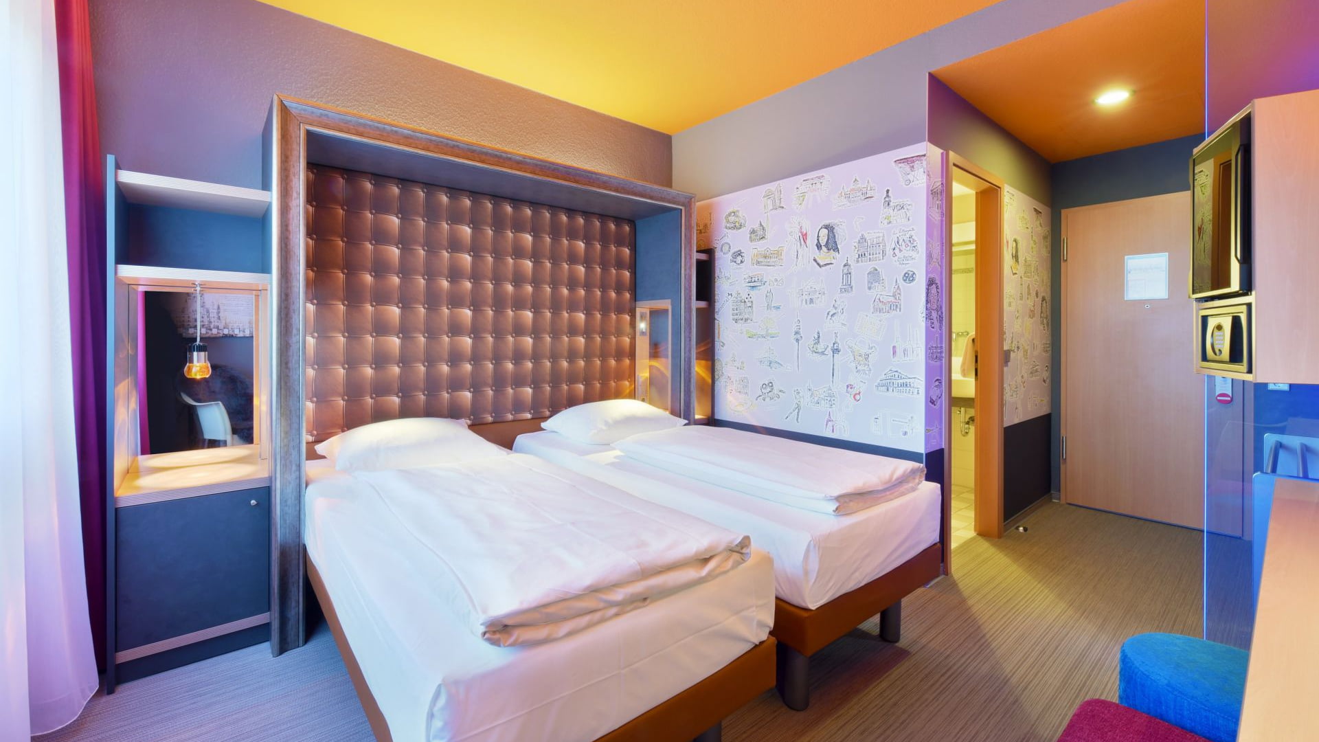 Einzelzimmer – Diagonalblick zu Bett und Eingangsbereich mit Eingang zum Bad. Zwei Einzelbetten, Safe in Augenhöhe