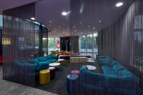 Designhotel-Lobby: Farbakzentuierte Lounge-Möbel und Sitzinseln hinter Fadenvorhängen