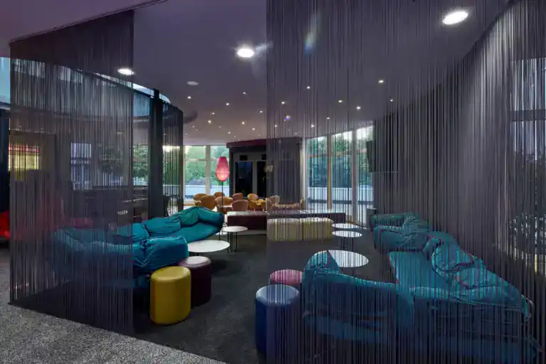Designhotel-Lobby: Farbakzentuierte Lounge-Möbel und Sitzinseln hinter Fadenvorhängen