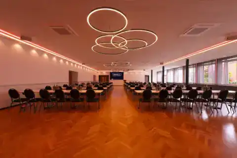 Kleiner Saal mit parlamentarischer Bestuhlung. Variable LED-Beleuchtung für verschiedene Veranstaltungstypen. Hier: Rot/Orange