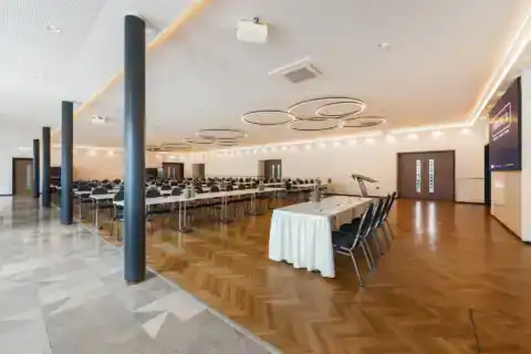 Kleiner Saal – Seitliche Perspektive. Parlamentarische Bestuhlung (bis zu 250 Personen), Präsidiumstisch vorne, LED-Display rechts, moderne Ringpendelleuchten, Fischgrätparkett mit angrenzendem Fliesenboden, visuelle Trennung durch vier Säulen