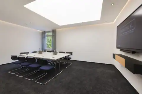 Tagungsraum VI – Diagonale Perspektive. Konferenztisch mit 10 Freischwingern, Display an der Wand, Oberlicht, ein Fenster, indirekte Beleuchtung, Teppichboden