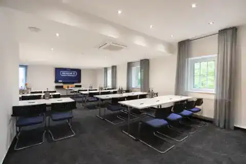 Conference room XI - frontal perspective. Parliamentary Seating arrangements with tables and 25 cantilever chairs, display on front wall, three windows on the right, recessed spotlights, carpeting