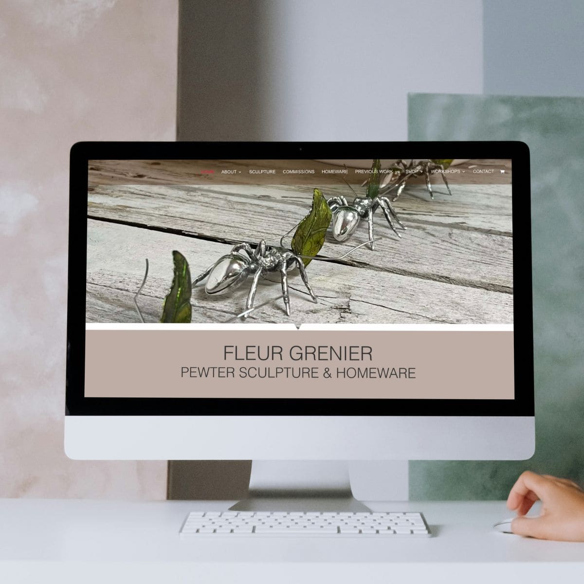 Computer screen displaying a website featuring pewter ant sculptures on wooden planks. The header reads Fleur Grenier Pewter Sculpture & Homeware. A persons hand is visible beside the monitor, highlighting why your website needs to be SEO-friendly to reach more art enthusiasts. Wildcurrant Marketing
