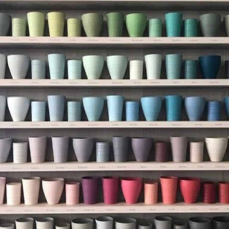 Green, blue, purple, pink, and gray ceramic plant pots on store shelves for gardening or home decor.
