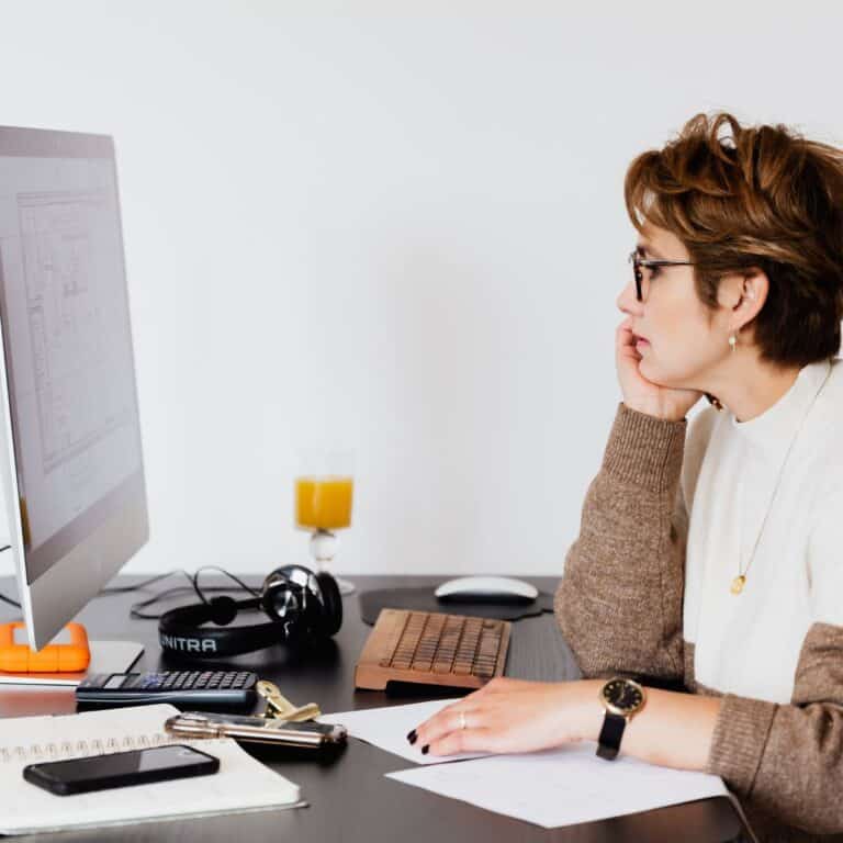 A woman working at a computer desk, asking questions about website design.