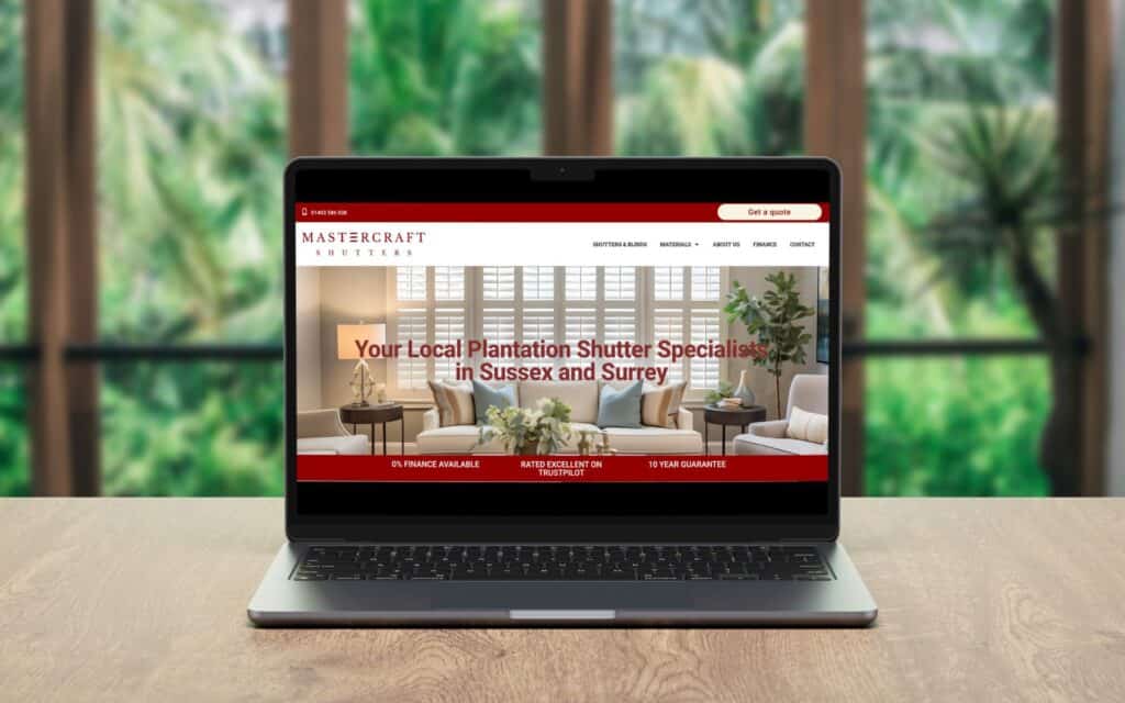 A laptop on a wooden table displays the Mastercraft Shutters website, which features an image of a living room with plantation shutters and the text: Your Local Plantation Shutter Specialists in Sussex and Surrey. Wildcurrant Marketing