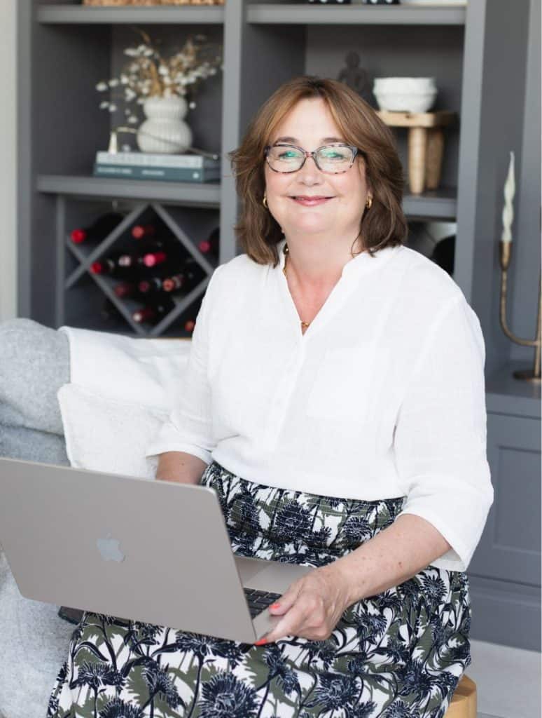 Smiling woman using a laptop at home, surrounded by stylish decor and books.