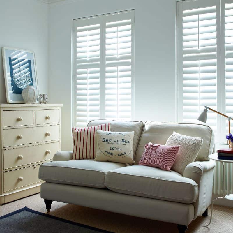Bright living room featuring white plantation shutters, a cream sofa, and decorative pillows, creating a light and inviting space.