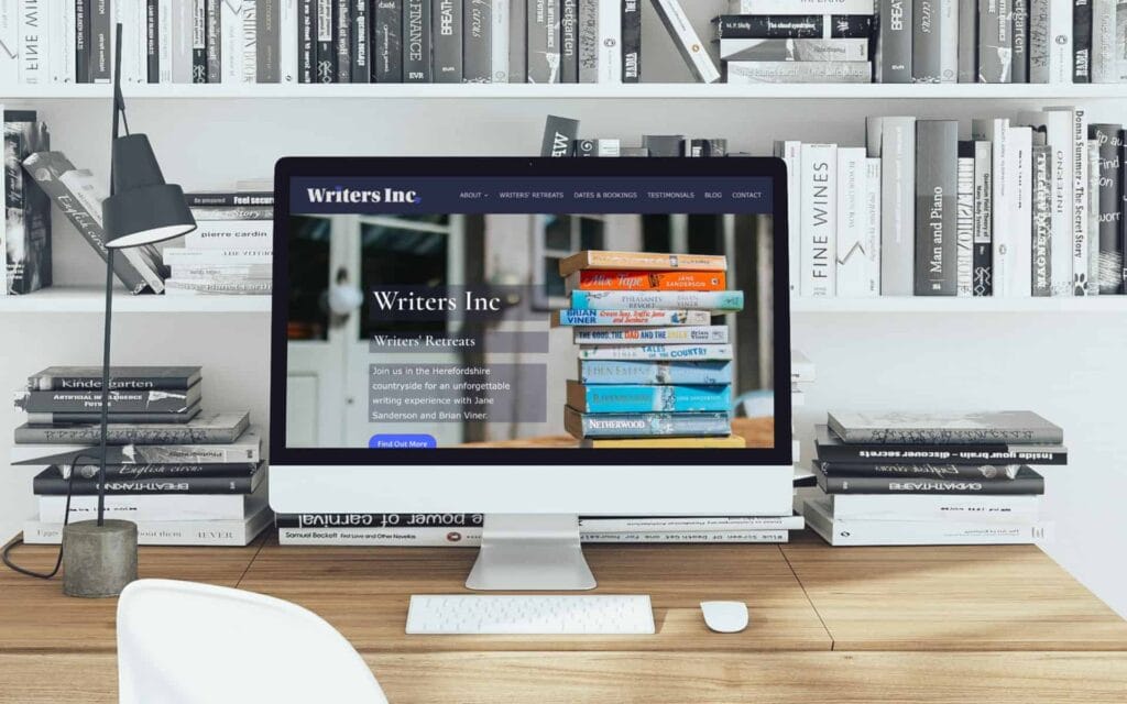 A computer monitor displaying a website about writers and books, on a wooden desk with bookshelves i.