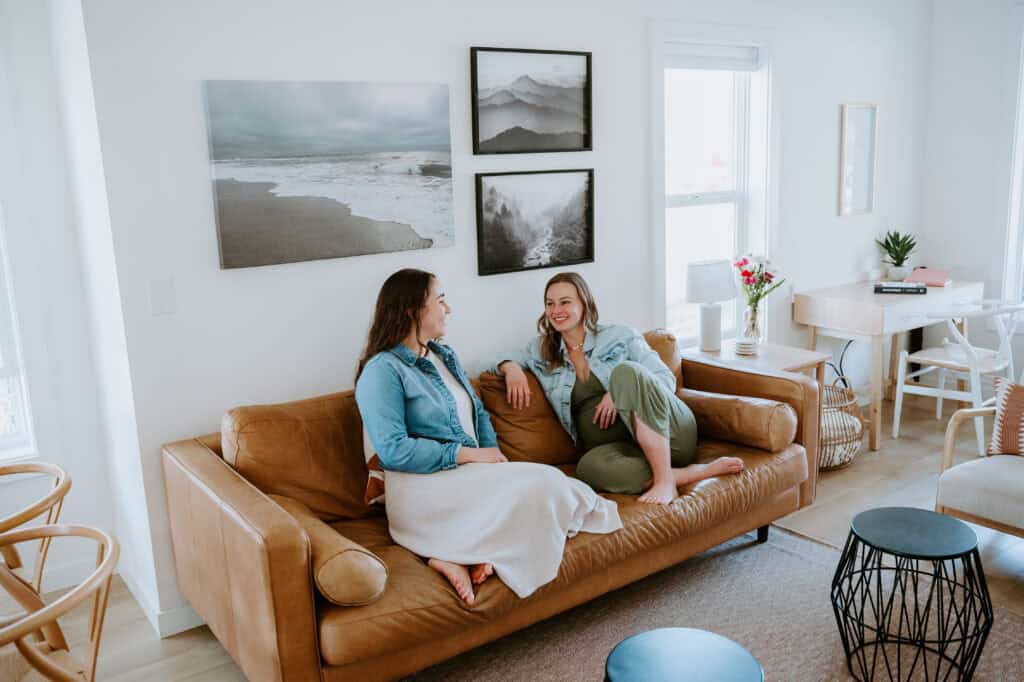 Two women chatting comfortably on a cozy living room sofa.