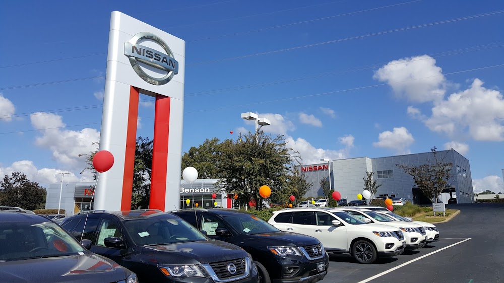 Nissan dealership with new cars lined up, balloons for promotions, and prominent Nissan sign under partly cloudy sky.