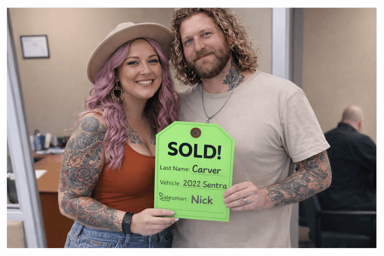 Tattooed couple smiles holding green "SOLD!" sign for 2022 Sentra at Willowood Ventures, with salesman Nick and Carver name shown.