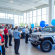 Automotive customers gather at a bright Willowood Ventures dealership, viewing a white Jeep SUV on display. Blue balloons, large showroom windows, and a festive atmosphere highlight the car-buying experience.