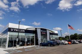 Modern car dealership with OFALLON sign, glass facade, parked vehicles, and American flag highlights Willowood Ventures’ auto marketing.