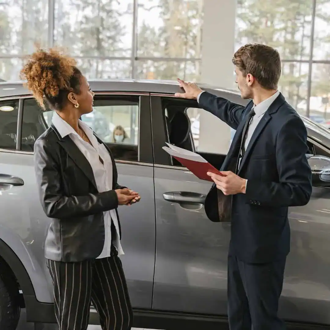Luxury car dealership sales consultation with a professional salesperson and female client.