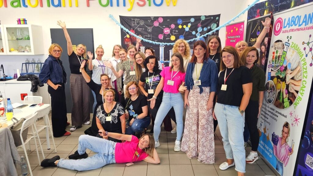 Witrynka w warsztatach edukacyjnych dla nauczycieli i wychowawców, promujących kreatywne metody nauczania i eksperymenty naukowe, z uśmiechniętymi uczestnikami i kolorowymi plakatami edukacyjnymi.