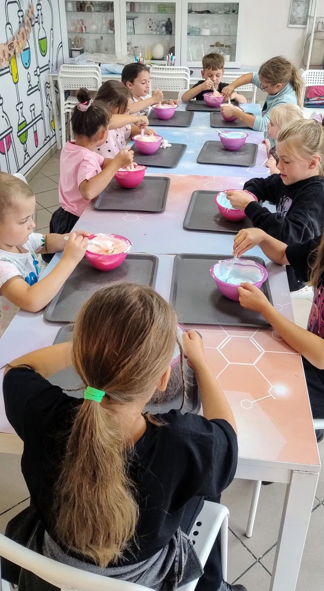 Różowe miski z masą cukrową na czarnych tackach, grupa dzieci podczas warsztatów cukierniczych, kreatywne zajęcia dla dzieci, edukacja kulinarna dla młodych adeptów, Wittlab, edukacja i warsztaty dla dzieci w kuchni.