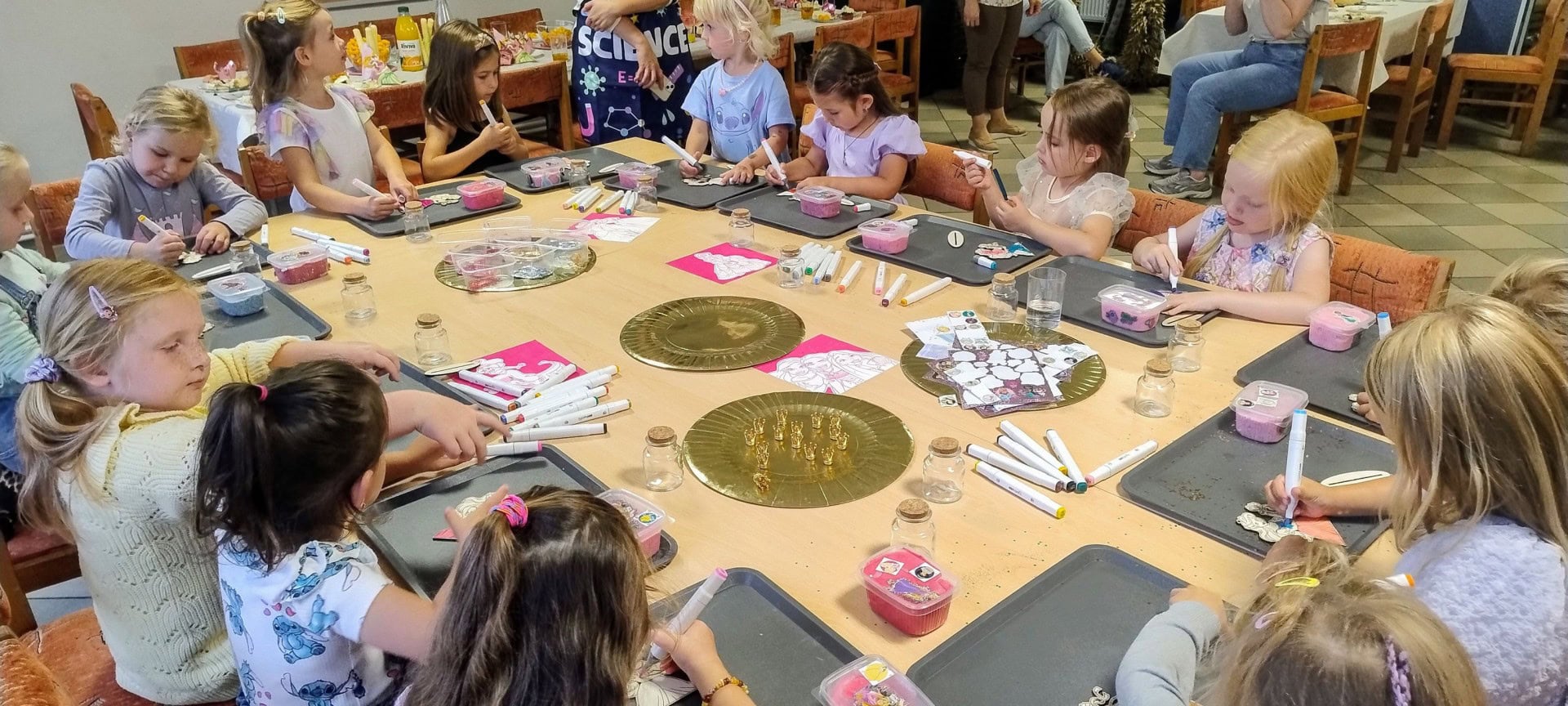 Kolorowe dzieci bawiące się i tworzące na warsztatach artystycznych w domu kultury Wittlab w Polsce. Uczestnicy korzystają z markerów, naklejek i innych materiałów podczas kreatywnych zajęć dla dzieci.