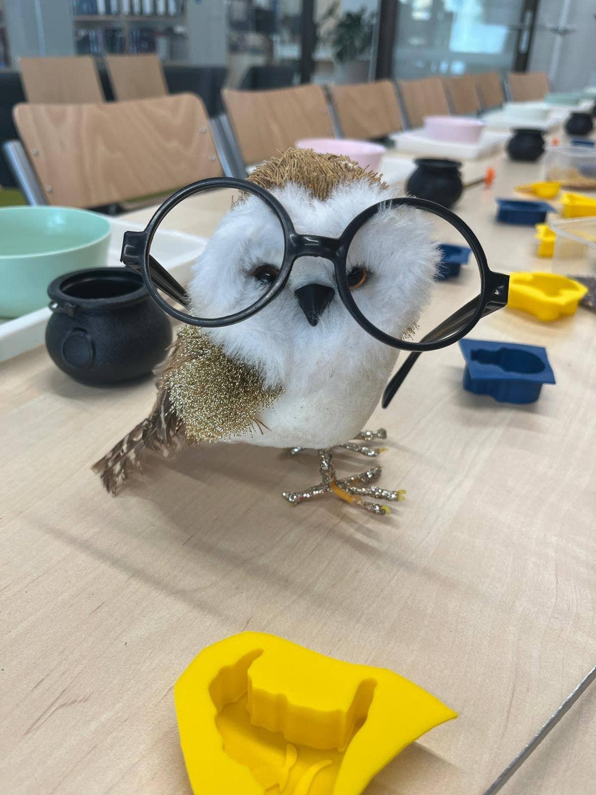 Artykuł doświadczalny w laboratorium, figurka ptaka ozdobnego z dużymi czarnymi okularami, otoczenie z kolorowymi ramek do odlewów i naczynia laboratoryjne, atmosfera nauki i kreatywności.