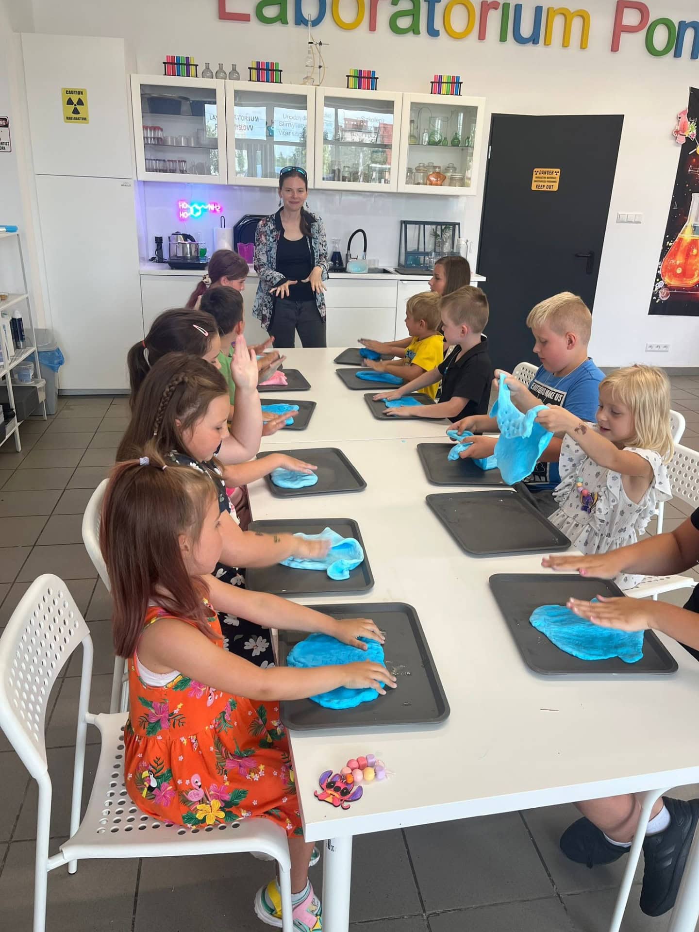 Kolorowe dzieci bawią się w Laboratorium, tworząc masę sensoryczną pod nadzorem nauczycielki w kreatywnym otoczeniu edukacyjnym.