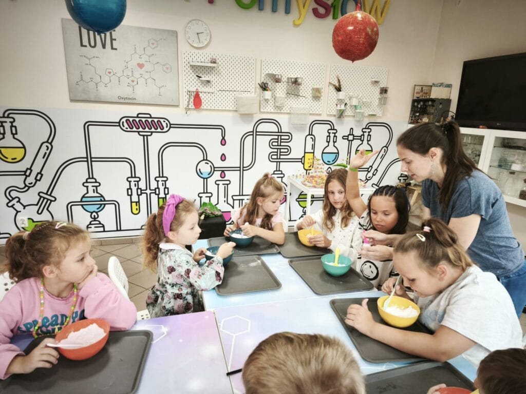 Przedszkolaki biorą udział w warsztatach naukowych, ucząc się przez zabawę w kreatywnej atmosferze, którą tworzy kolorowa ściana z ilustracjami laboratoryjnymi w nowoczesnym centrum edukacyjnym Wittlab.