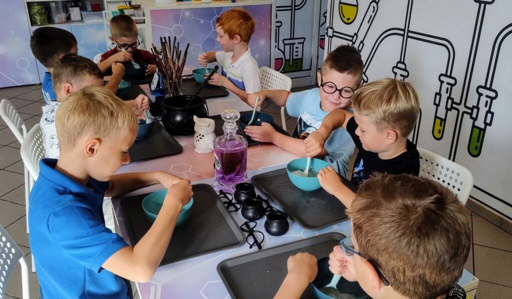 Kolorowa grupa dzieci w laboratorium chemicznym, uczące się i eksperymentujące z różnymi próbkami i chemikaliami, w profesjonalnej przestrzeni edukacyjnej.