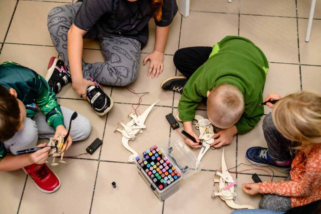 Ludzie uczący się programowania robotów na podłodze, składanie i przełączanie robotów edukacyjnych, rozwijanie umiejętności STEM, zabawa z edukacyjnymi robotami dla dzieci.