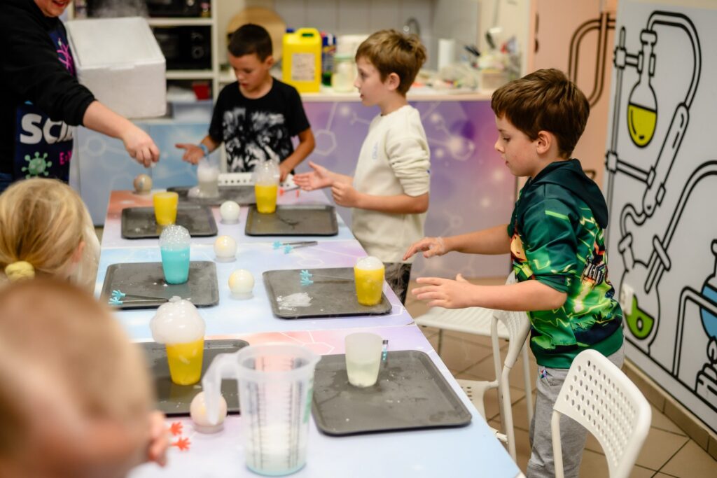 Kolorowa edukacyjna stacja naukowa dla dzieci, warsztaty chemiczne z udziałem młodych uczestników, eksperymenty z reakcjami chemicznymi i przyrządami laboratoryjnymi, atrakcyjne zajęcia edukacyjne w centrum nauki.