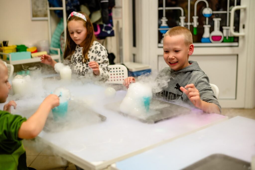 Kolorowe eksperymenty naukowe z suchym lodem, dzieci w laboratorium, edukacja chemiczna, zabawy naukowe dla dzieci, nauka przez zabawę na warsztatach dla dzieci.