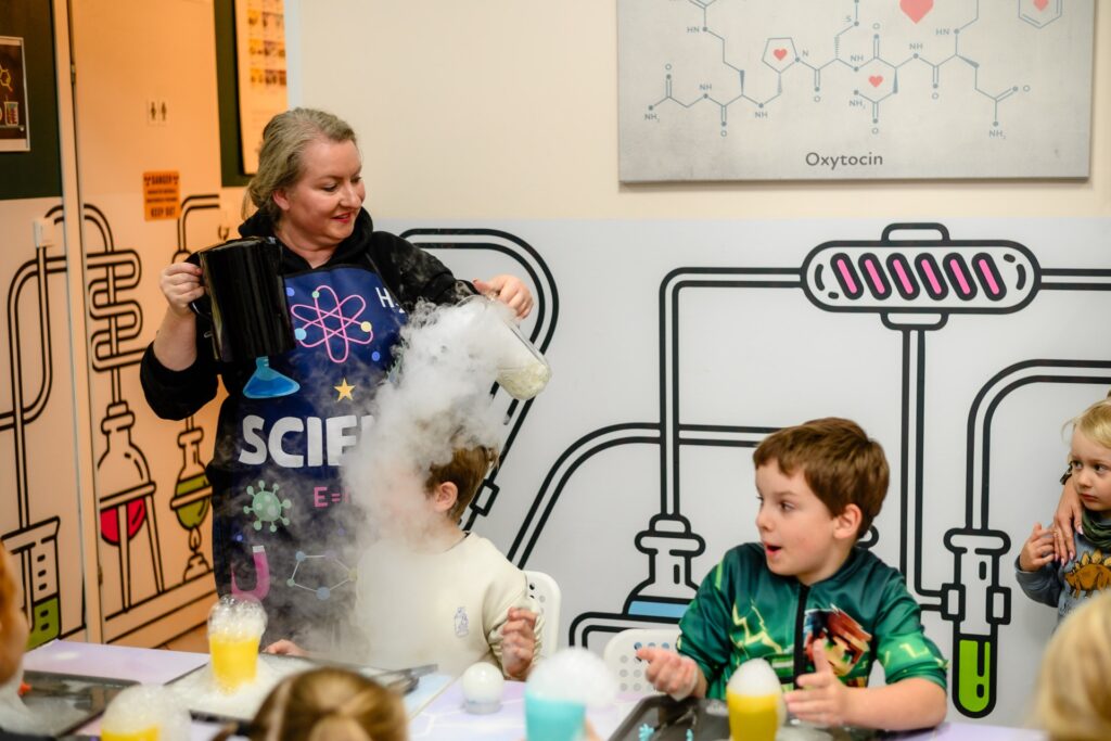 Kolorowe eksperymenty chemiczne dla dzieci w warsztatach naukowych, pokaz dymu suchy lód w laboratorium edukacyjnym, nauka przez zabawę, inspirujące zajęcia dla młodych naukowców, edukacja STEM.