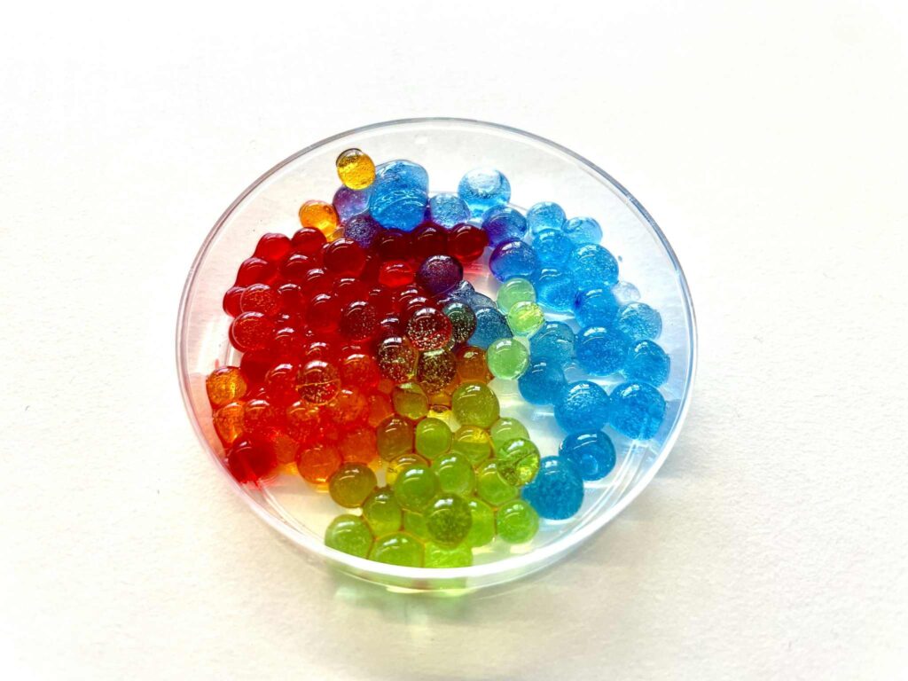 Kolorowe kuleczki żelowe w przeźroczawym naczyniu, różnorodne kolory, popularne jako żele do kontaktów lub ozdoby.