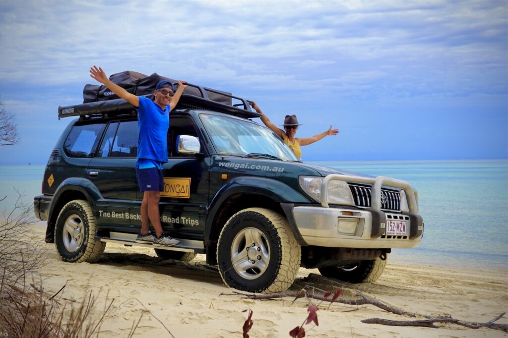 Wongai 4wd Hire - car on beach with people hanging onto the vehicle