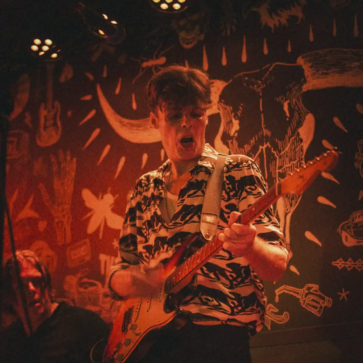 Young musician playing electric guitar at Belushi's during World Cup event.