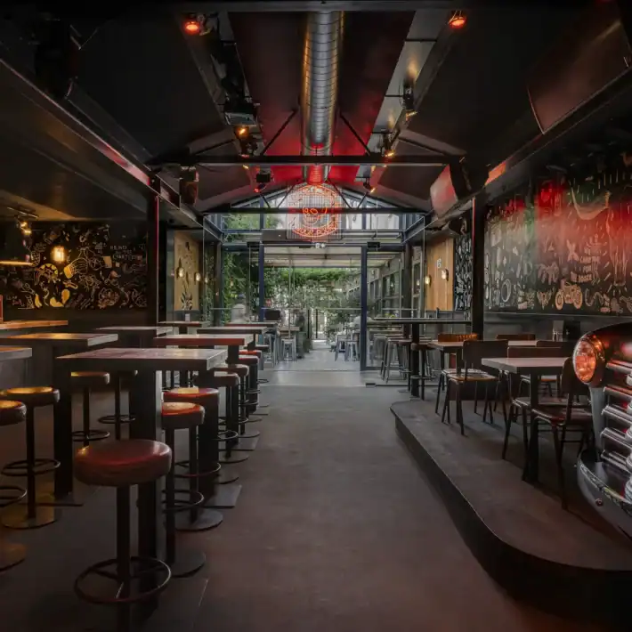 Interior of a modern bar with high tables and stools, decorated with colourful murals.