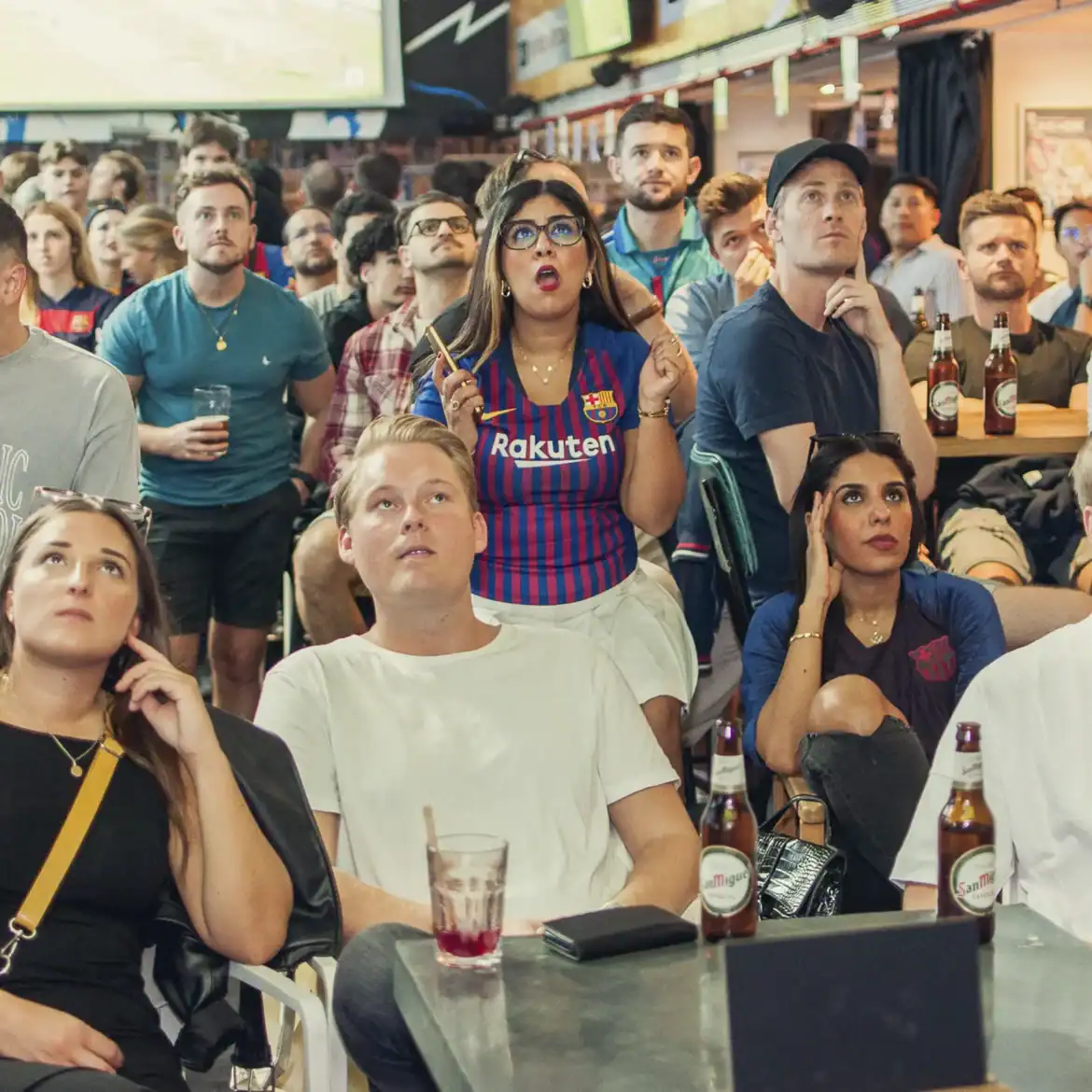Crowd of football fans watching live match at Belushi's pub.