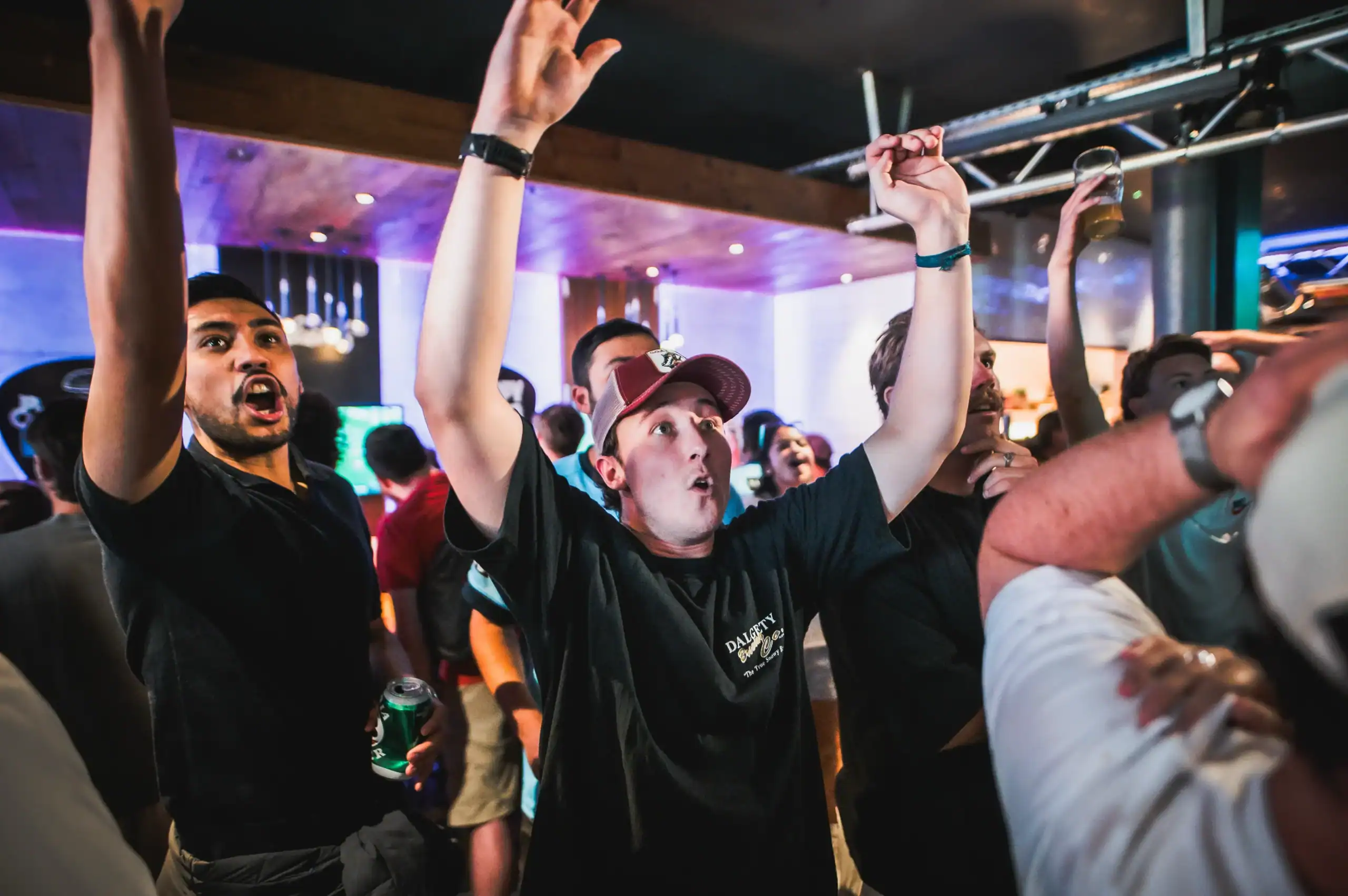 Packed crowd at Belushi's sports bar with arms raised watching the World Cup live, the electric atmosphere that only a room full of passionate football fans can generate
