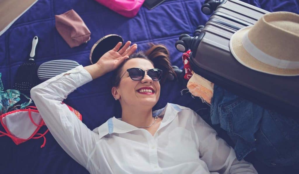 Beautiful woman relaxing with travel essentials on bed, ready for vacation or trip, embodying the travel and adventure spirit.