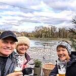 Shared memories on a Tauck Small Ship Cruise. Cruise participants enjoying drinks by the riverside in a scenic European town, showcasing travel experiences with friends, picturesque waterfront, and casual outdoor dining in a charming setting.