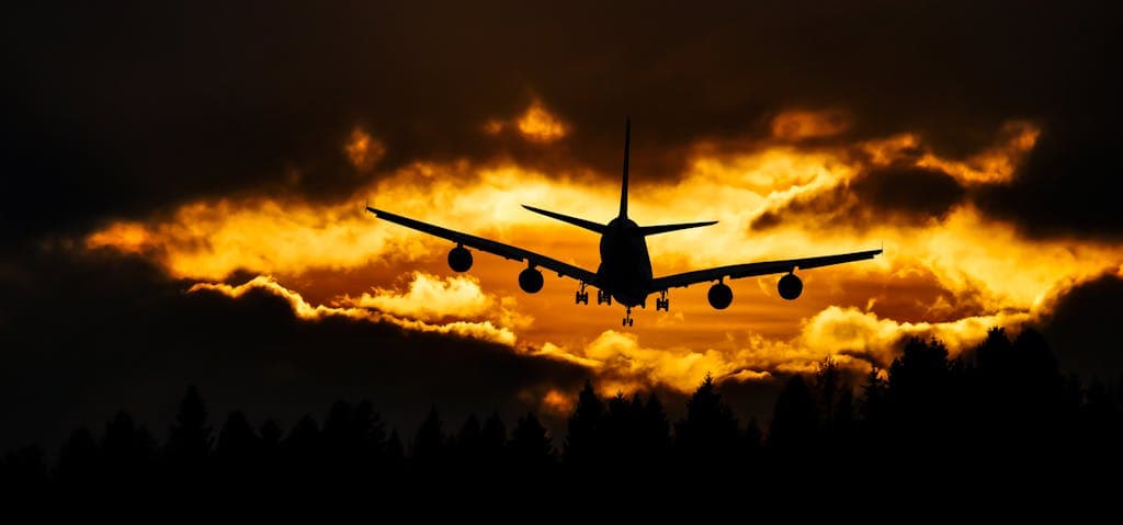 Silhouette of an airplane flying across a vibrant sunset sky, symbolising the start of a WorldLee Journeys bucket list adventure.