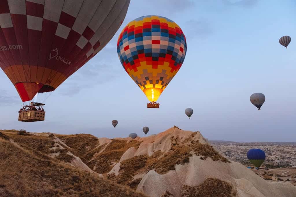 Breathtaking view of colorful hot air balloons soaring over Cappadocia's unique landscape at sunrise. A must do experience in Cappadocia.