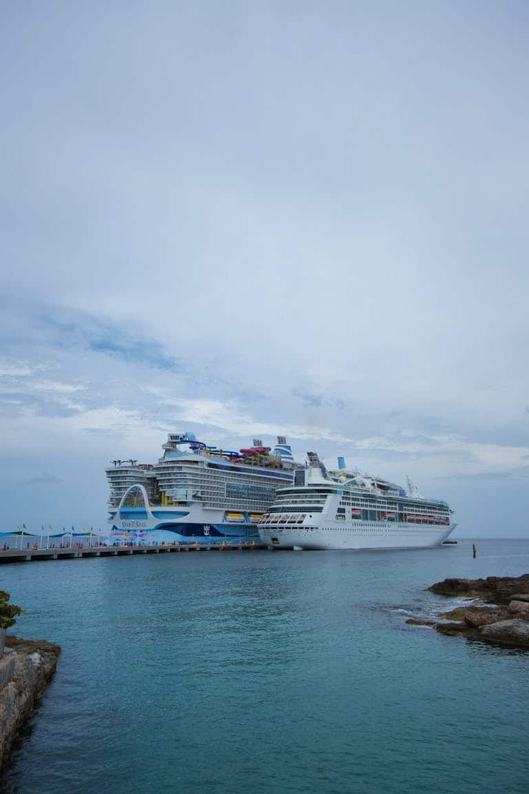 Two different sized luxury cruise ships docked at a pier in the Bahamas under a cloudy sky. Small Ship Cruising vs large ship cruising.