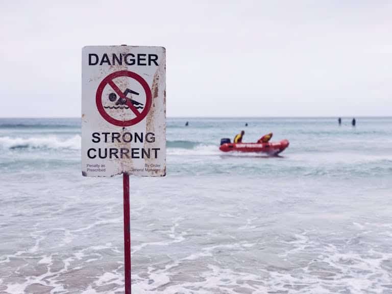 Is Australia Safe? It is if you follow warning signs like this sign for strong currents at Gold Coast, Australia. Lifeguard boat visible in background.