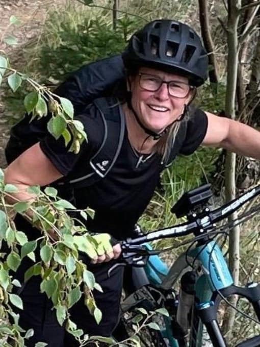 Frau mit Helm und Brille beim Mountainbiken im Grünen.