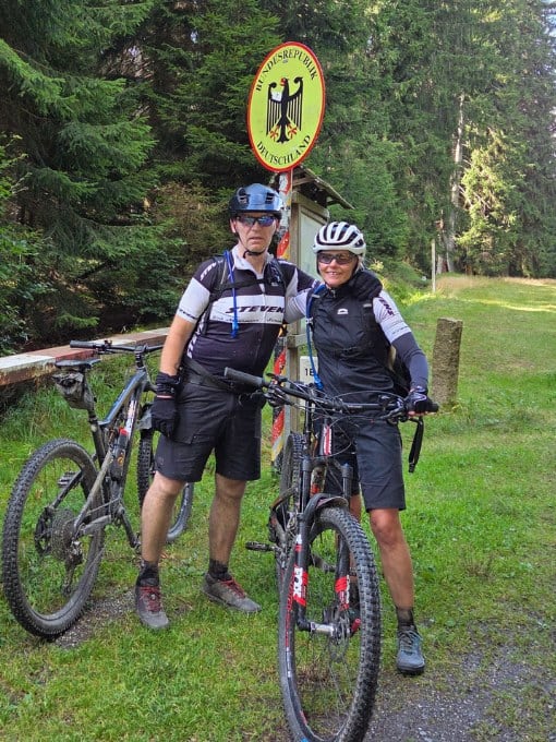 Zwei Radfahrer mit Helm und Fahrrad vor Deutschland-Flagge im Wald.