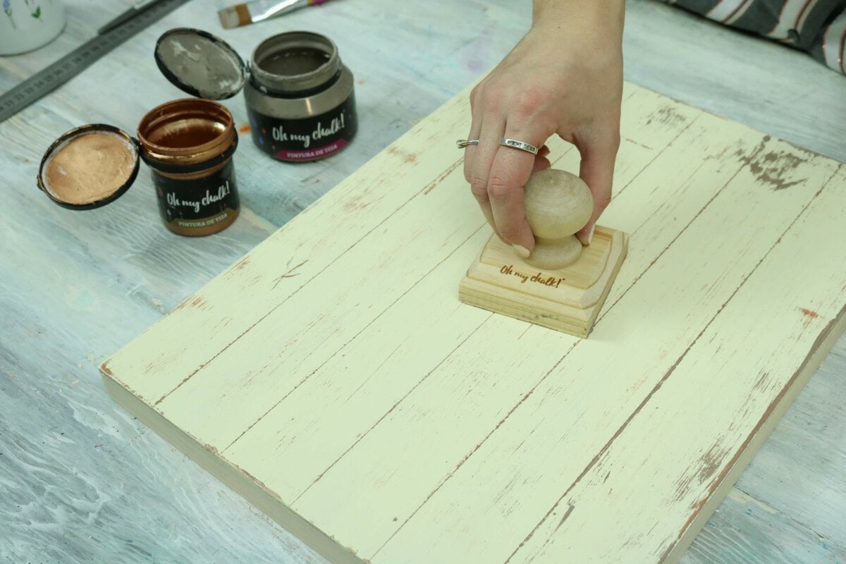 Madera pintada en color crema con sello de goma grabado con la frase "Oh my chalk!" sobre una mesa de trabajo, proceso de decoración de madera artesanal.